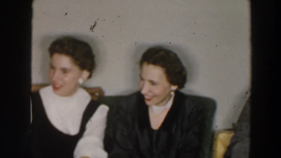 1957 home-movie frame from metadata-identified Wheeling, Ohio, showing two women laughing together in a private indoor setting.