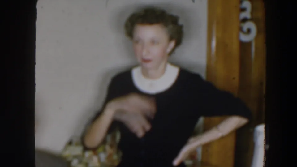 The woman appears mid-conversation in the 1957 home movie, one hand blurred in motion near her chest.