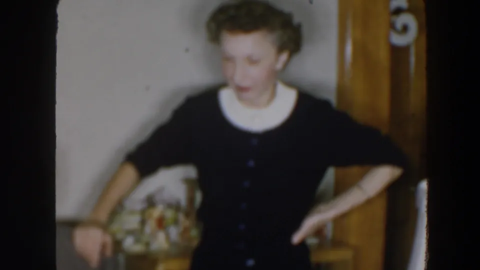 In a soft 8mm frame, the woman looks down while standing by a wall and wooden interior trim in Wheeling, Ohio.
