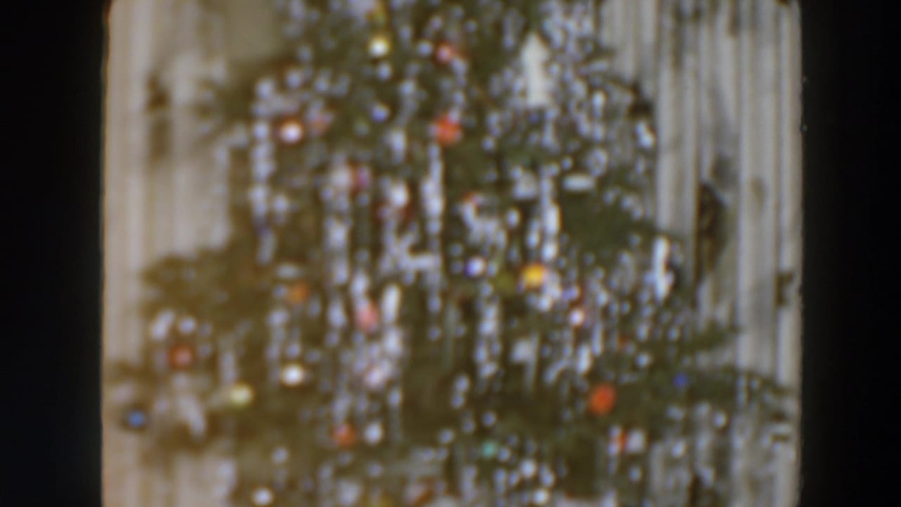 A softly focused Christmas tree with colored bulbs appears beside pale curtains in the 1957 home-movie footage.