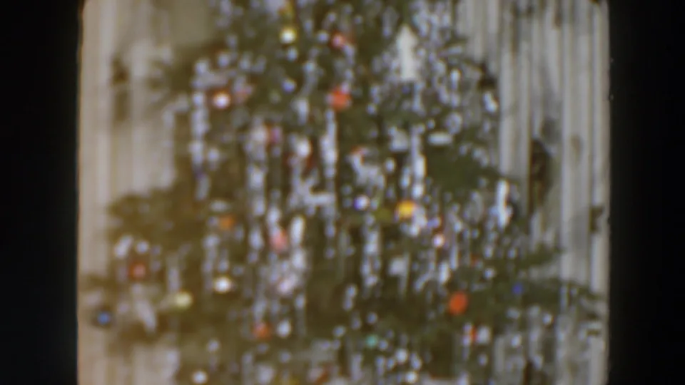 A softly focused Christmas tree with colored bulbs appears beside pale curtains in the 1957 home-movie footage.