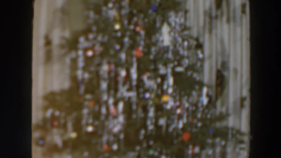 The 1957 8mm frame shows a blurred decorated Christmas tree with small colored lights and pale vertical background lines.