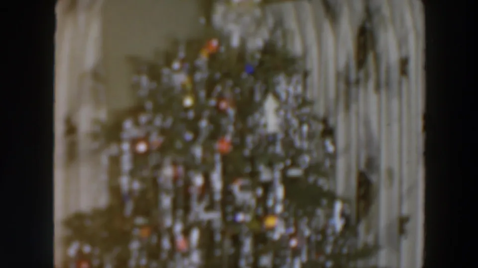 1957 home-movie view of a decorated Christmas tree with shimmering tinsel and colored ornaments or lights against pale curtains.