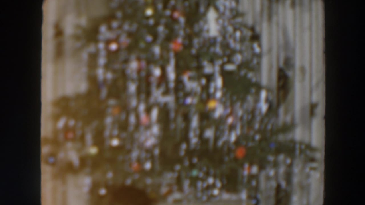 Decorated Christmas tree with bright ornaments beside a pale interior wall.