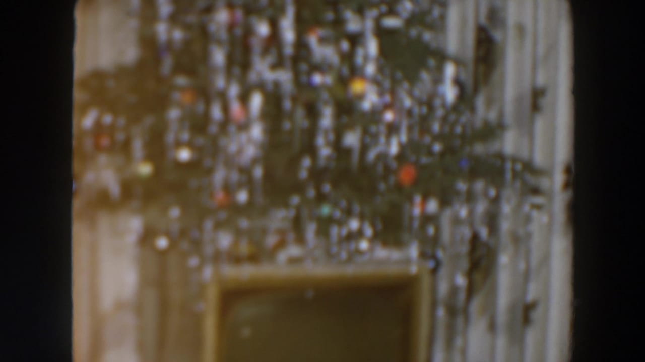 Christmas tree with ornaments above a low piece of furniture against a pale wall.