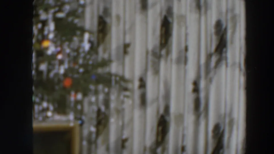 Final 1957 8mm frame shows the decorated Christmas tree near a wall and low furniture, with dark borders from the scanned film.