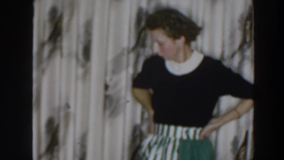 Woman in a dark top and striped skirt looks down off frame in a private Wheeling home interior during the Christmas clip.
