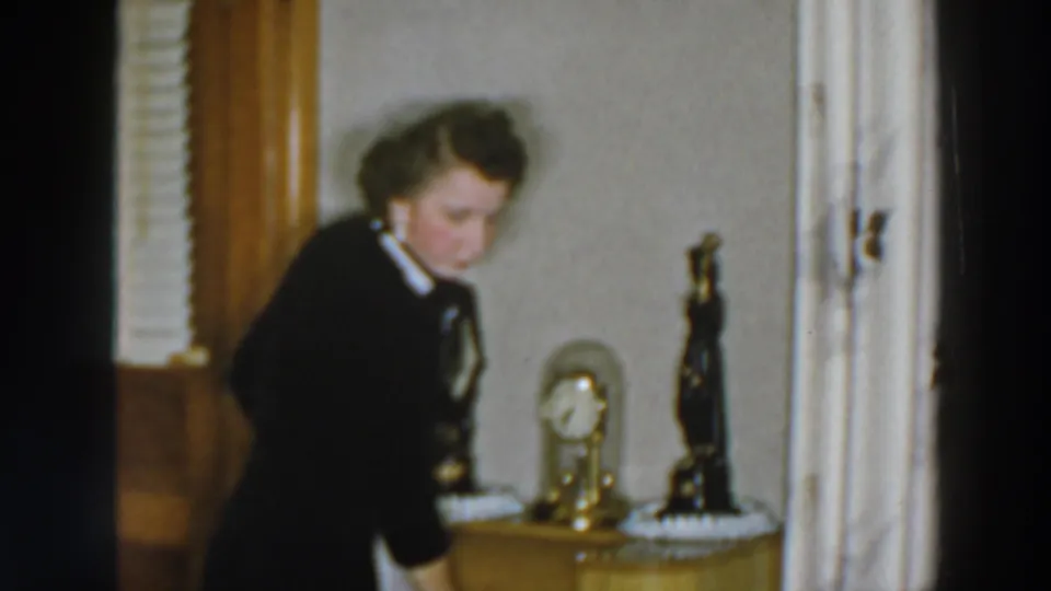 Near the end of the clip, the woman stands in the Wheeling, Ohio room beside a small clock and dark statuette after searching the drawer area.