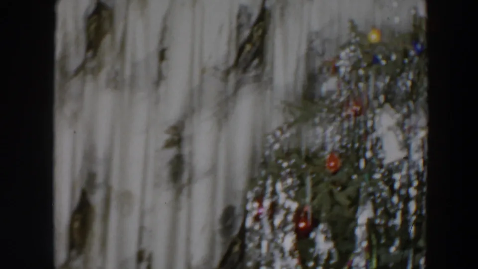 Decorated Christmas tree with silver tinsel and red ornaments appears beside light curtains in the 1957 home movie.