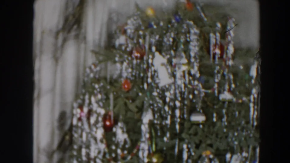 Close 8mm frame of a Christmas tree with silver tinsel, red ornaments and pale garland in a domestic setting.