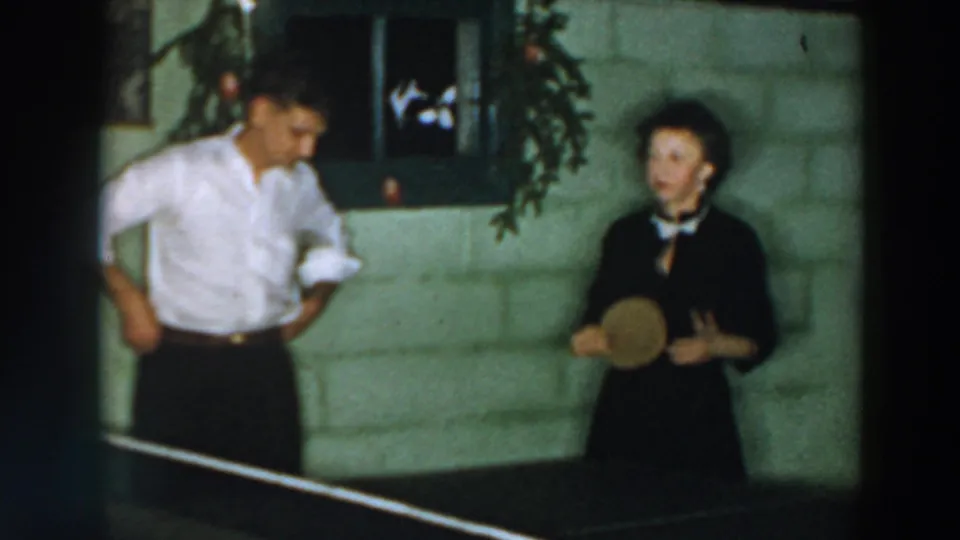 Two adults appear beside a ping pong table in the 1957 Wheeling, Ohio holiday home-movie scene.