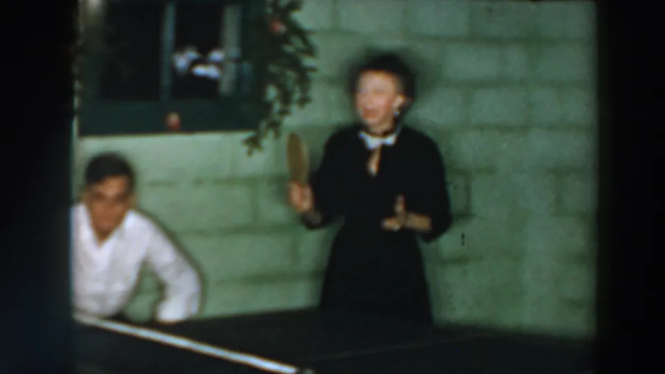 A woman with a paddle and a seated man are shown during indoor ping pong in the 1957 Wheeling, Ohio clip.