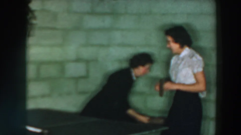 Two adults are captured mid-play near a ping pong table in the 1957 Wheeling, Ohio home-movie footage.