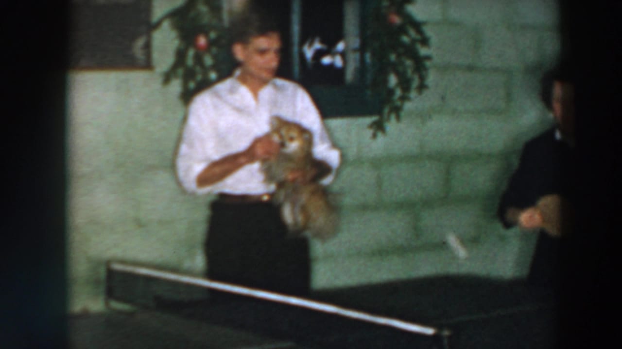 Man in a white shirt holds a small dog beside a ping pong table.