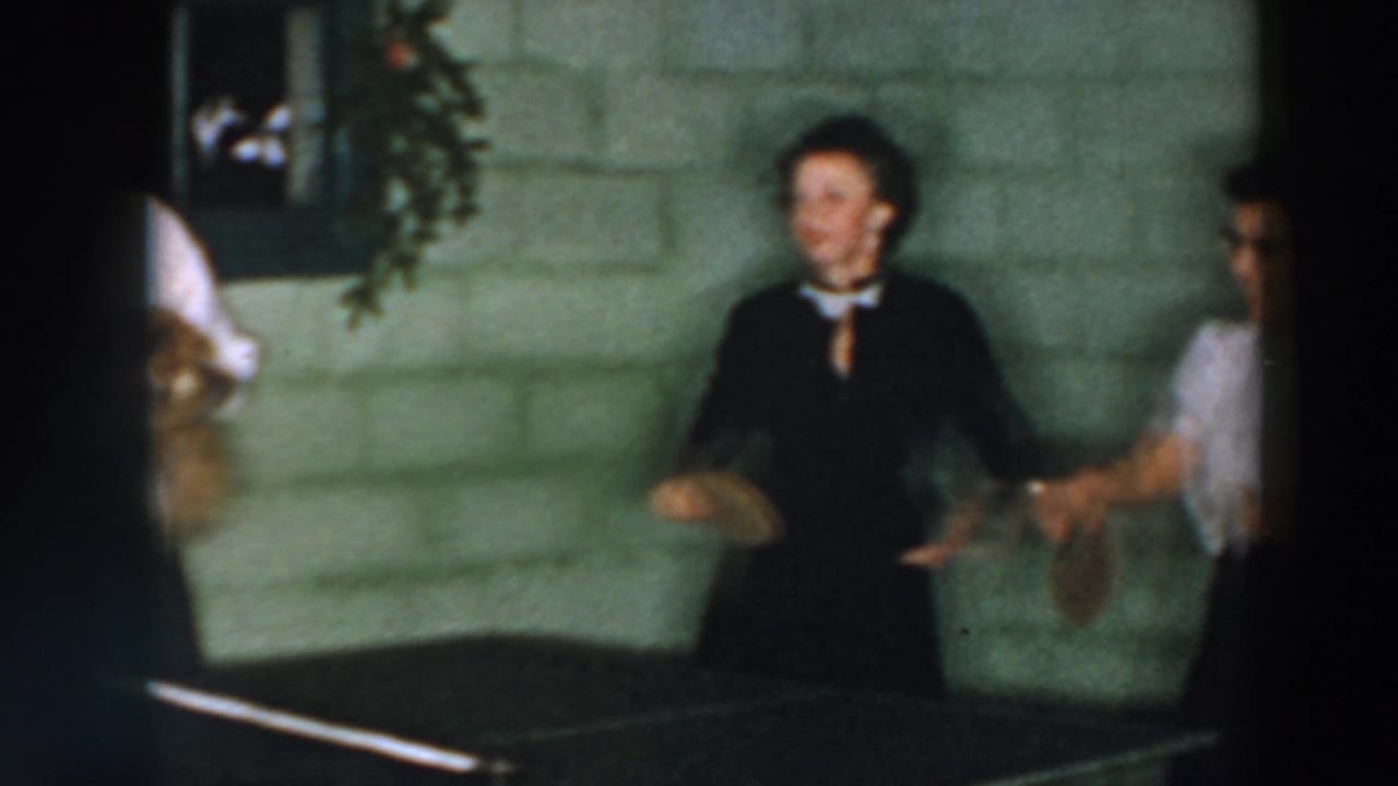 Two adults stand near a ping pong table, one holding a paddle.