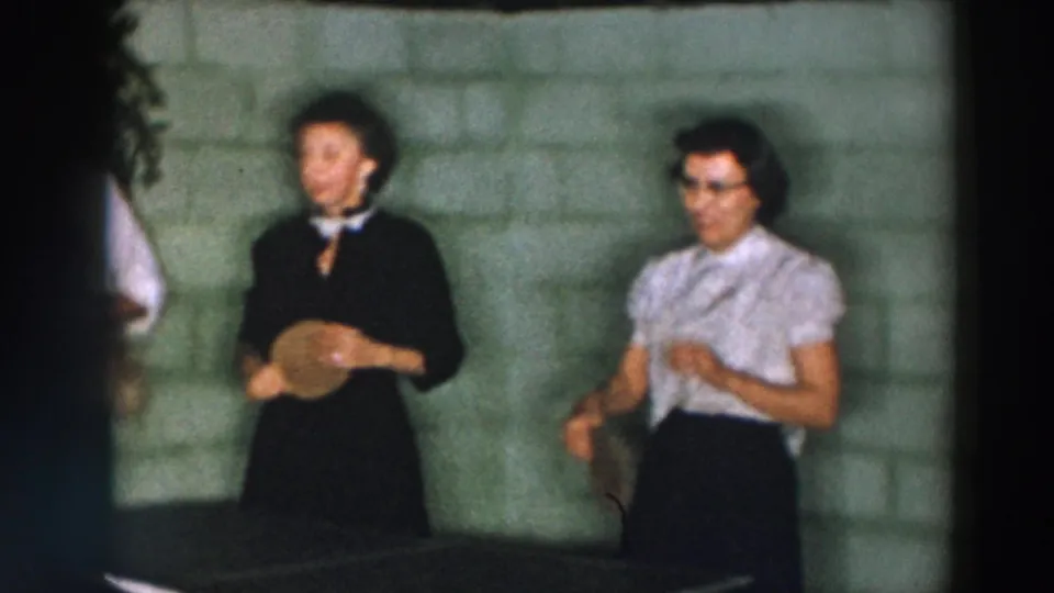 Two women in mid-century dress stand beside the ping pong table in the Wheeling, Ohio home-movie scene.