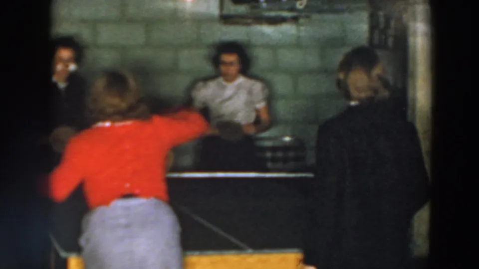 1957 Wheeling, Ohio 8mm frame with a woman in red reaching during a basement table tennis game.