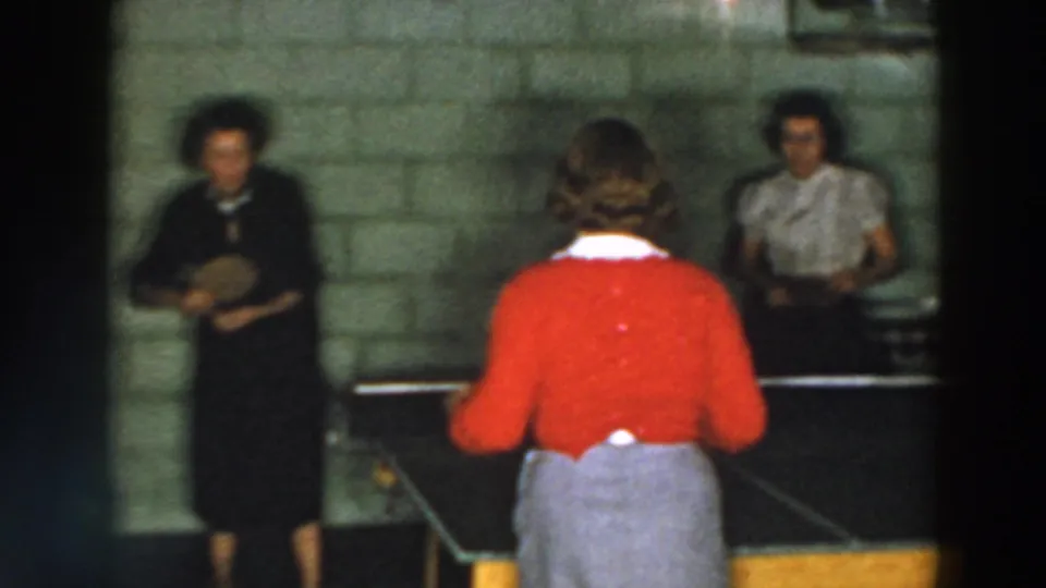 A 1957 home-movie still from Wheeling, Ohio showing women at a ping pong table in a cinder block room.