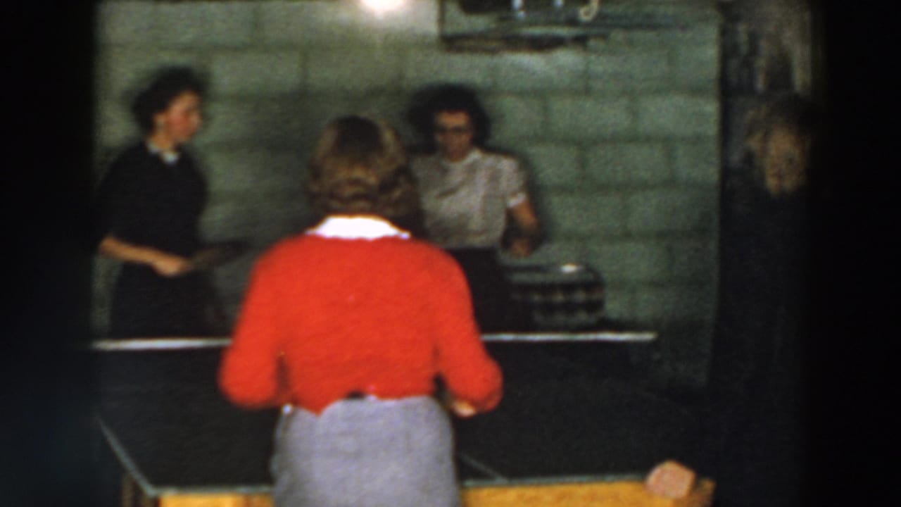 A woman in a red sweater faces two women across a table tennis table.