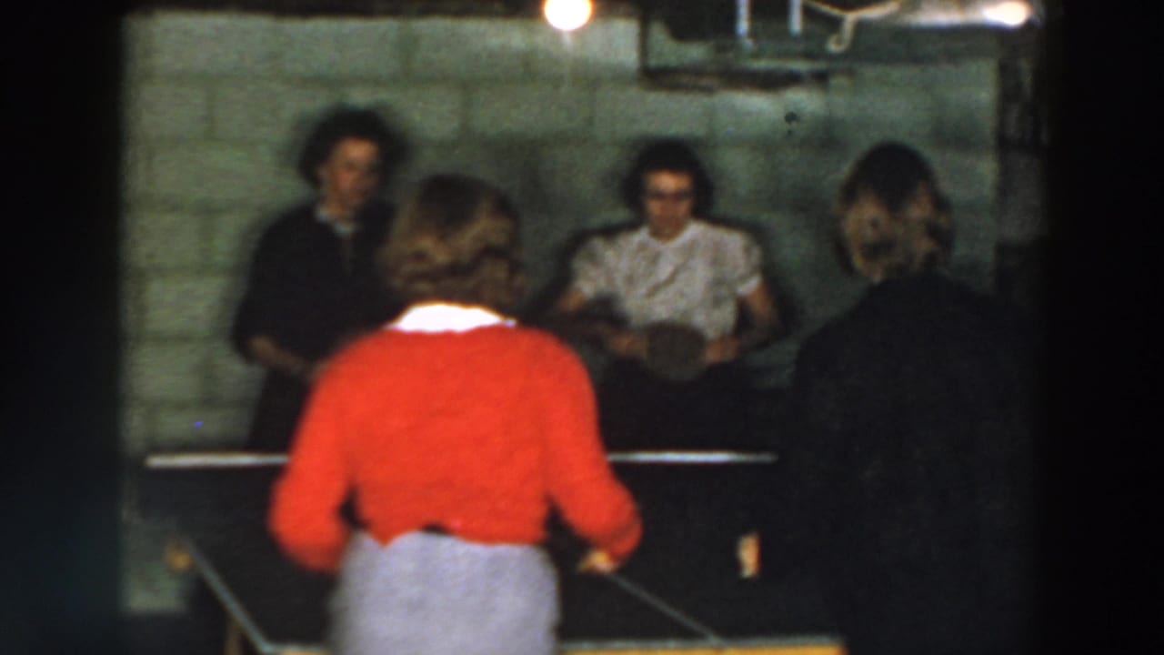 Four people around a table tennis table in a basement, with a red-sweatered player in the foreground.