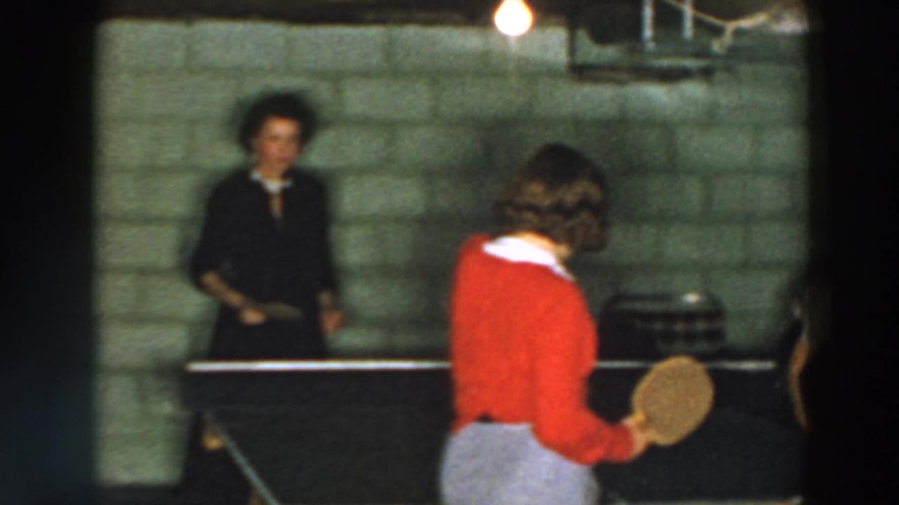 Basement table tennis scene from the 1957 Wheeling home movie, with a player in red and another figure across the table.