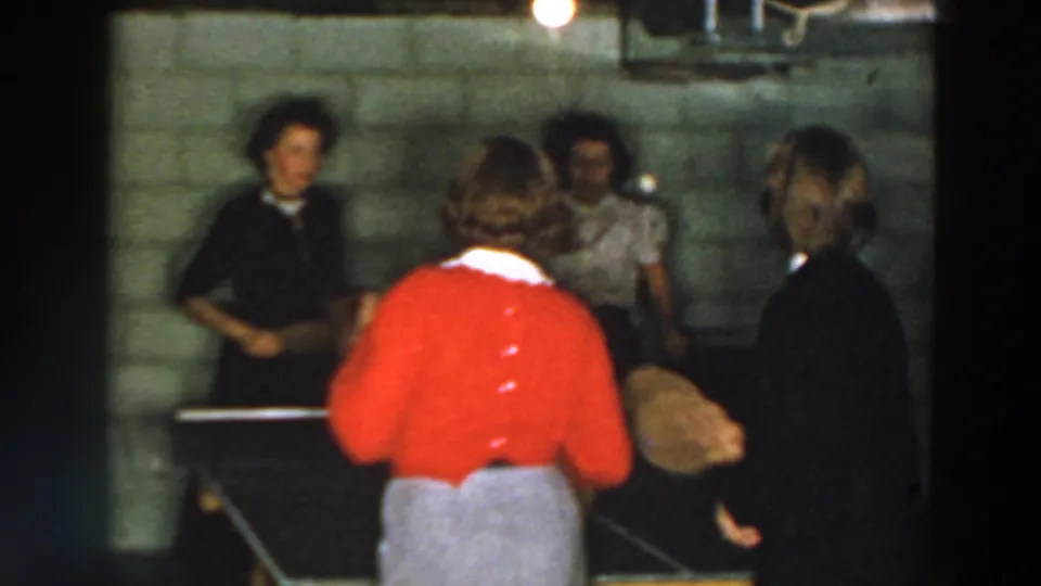 1957 Wheeling basement recreation frame with a red-sweatered table tennis player and onlookers in soft 8mm color.