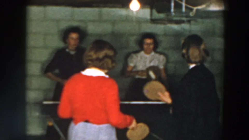 Wheeling, Ohio 1957 home-movie frame showing an informal basement table tennis game with four visible people.