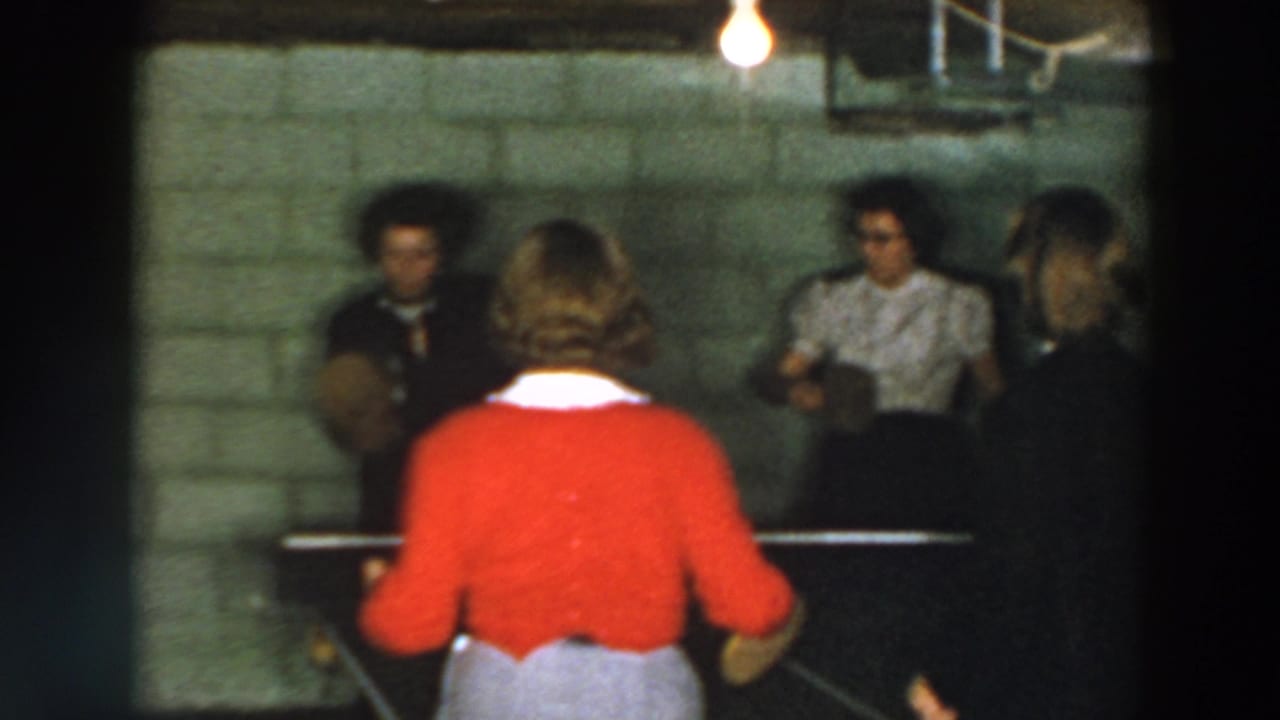 Young women play table tennis in a basement with a cinder block wall and exposed bulb.