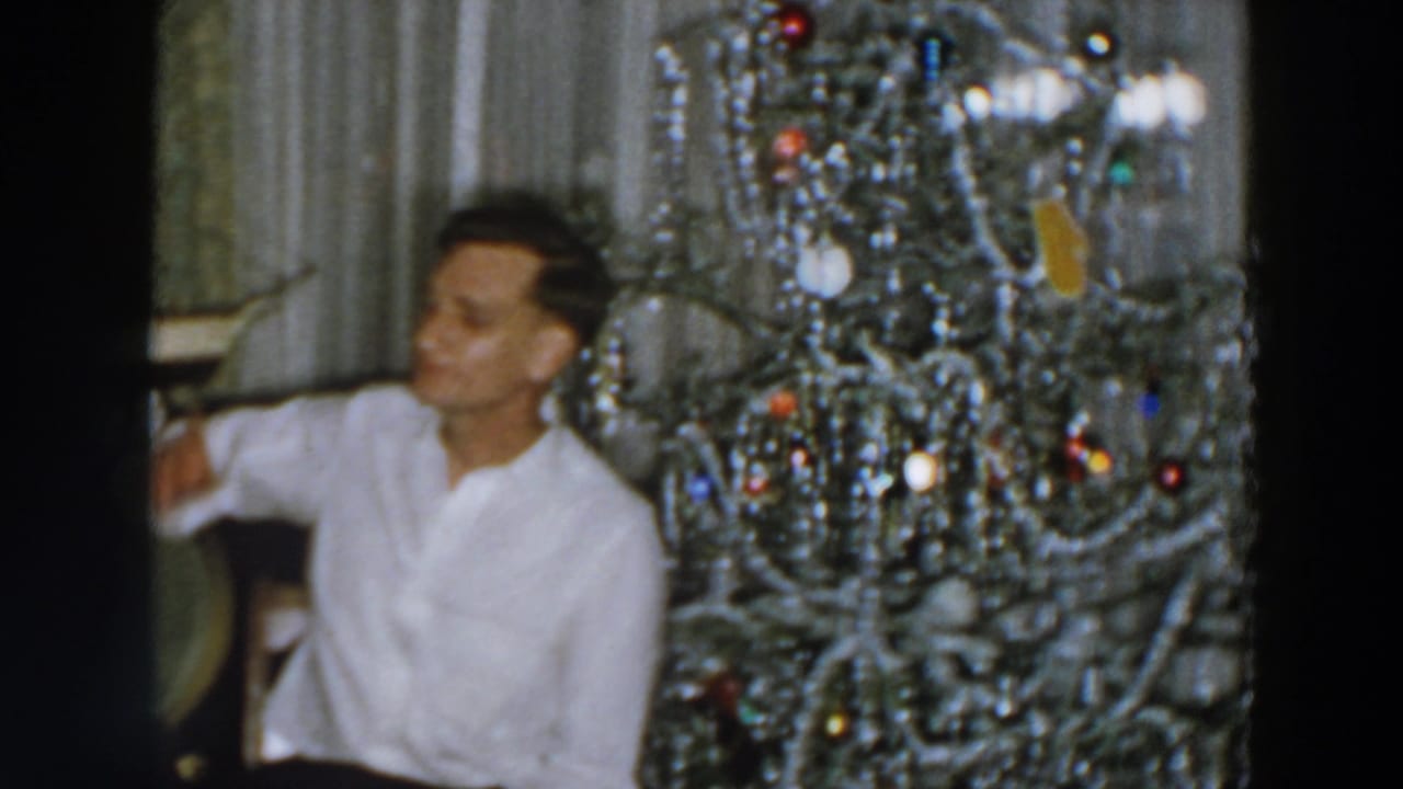 Man turns toward the side while seated near a decorated Christmas tree.
