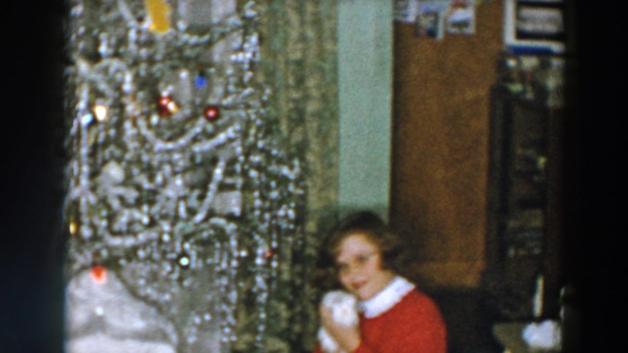 1957 Wheeling, Ohio home-movie frame showing a woman in a red sweater beside a silver Christmas tree with a small white pet.