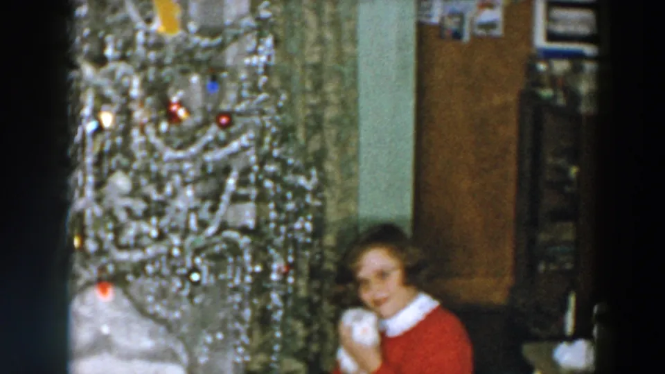 1957 Wheeling, Ohio home-movie frame showing a woman in a red sweater beside a silver Christmas tree with a small white pet.