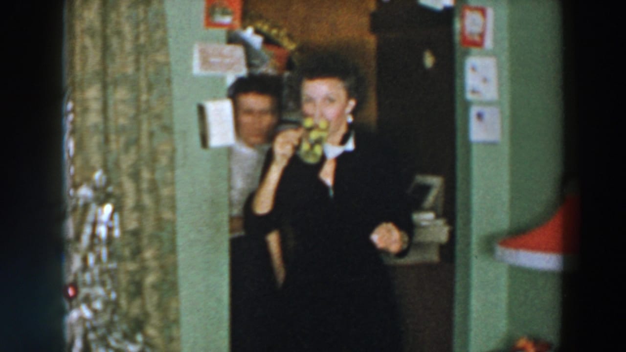 Woman in a dark dress drinking from a patterned mug near a doorway and holiday decorations.