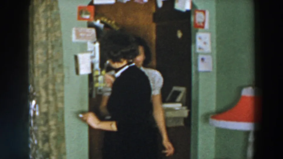 1957 Wheeling, Ohio home-movie frame of two women moving past one another in a Christmas-decorated private room.