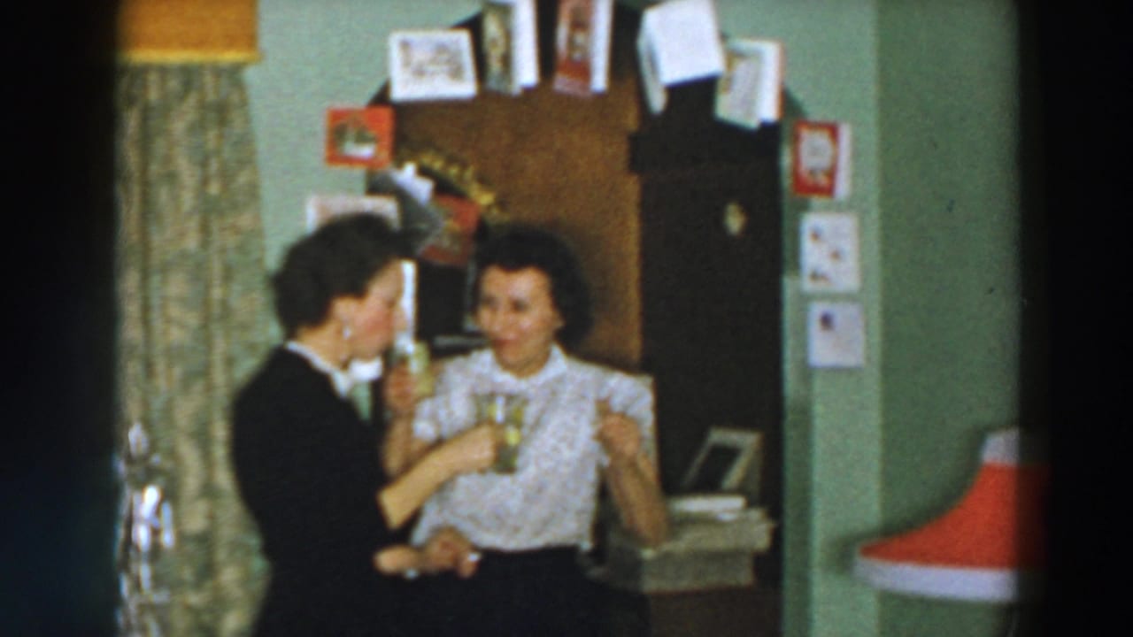 Two women smile indoors while holding patterned mugs near a doorway.