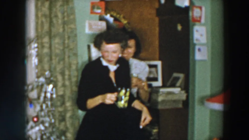 Near the end of the 1957 Wheeling Ohio clip, one woman smiles toward the camera as her companion stands partly behind her indoors.