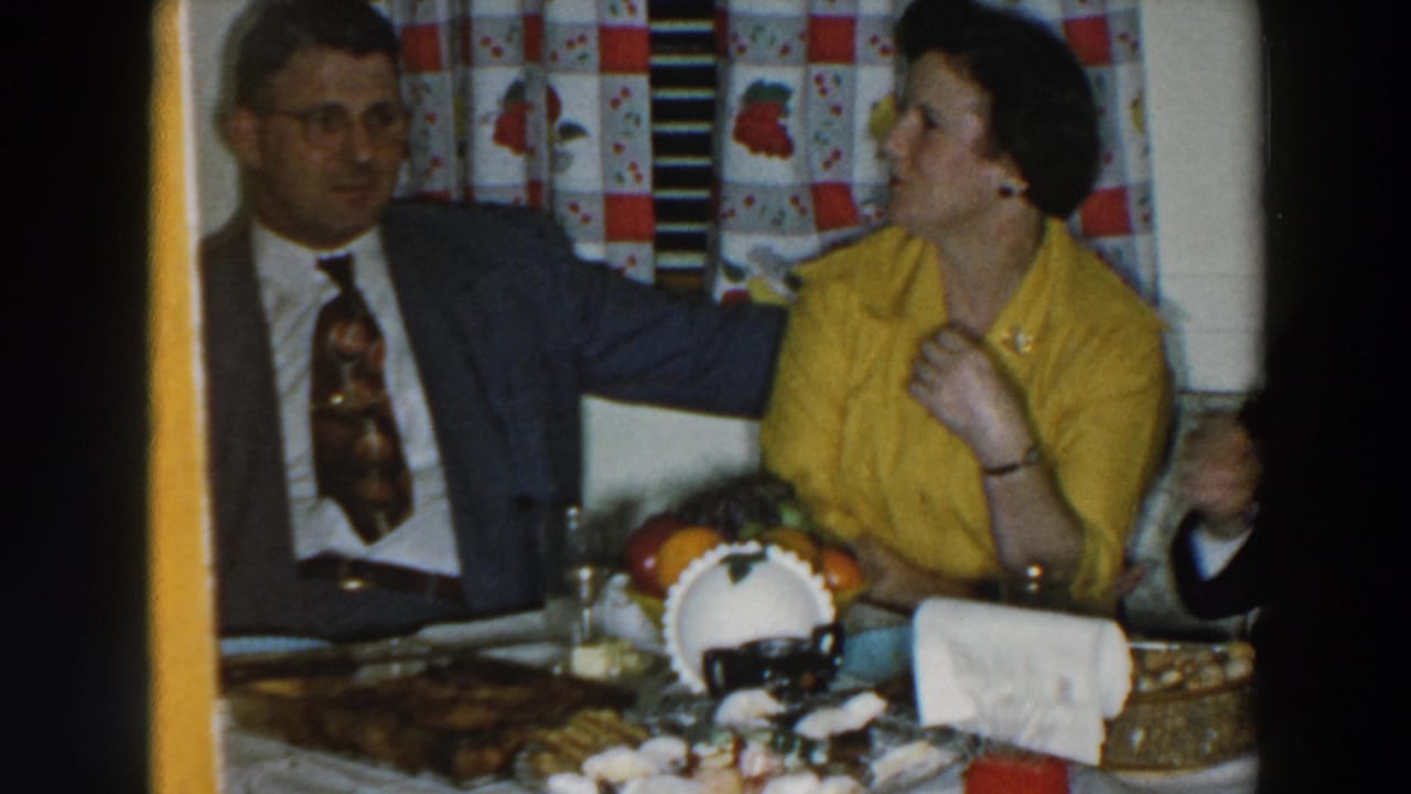 Man in a suit sits beside a woman in a yellow blouse at a table with food.