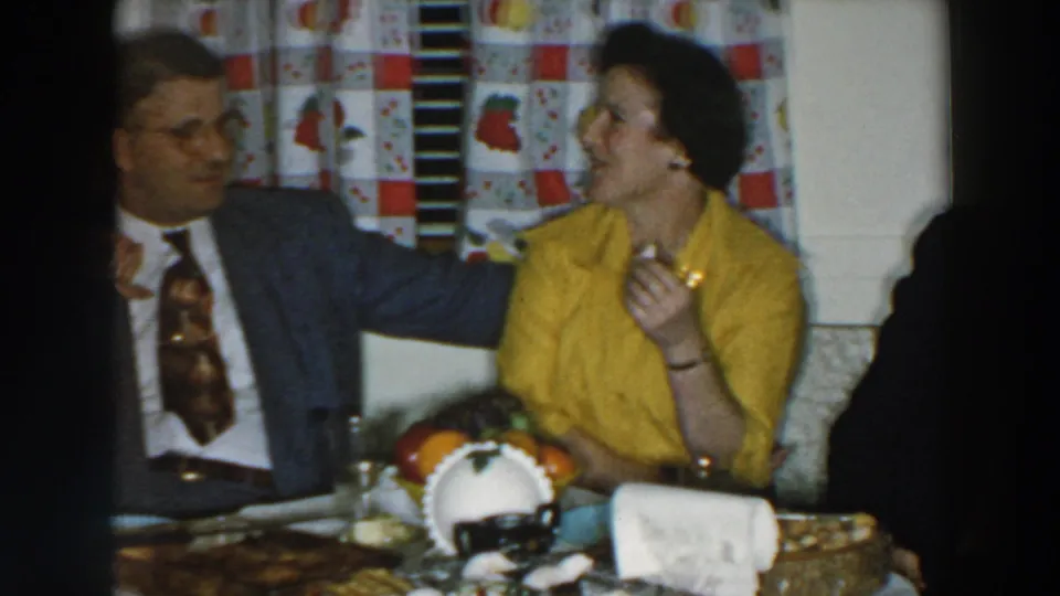 1957 Wheeling, Ohio home-movie frame of two adults in conversation beside a table set for a social meal.