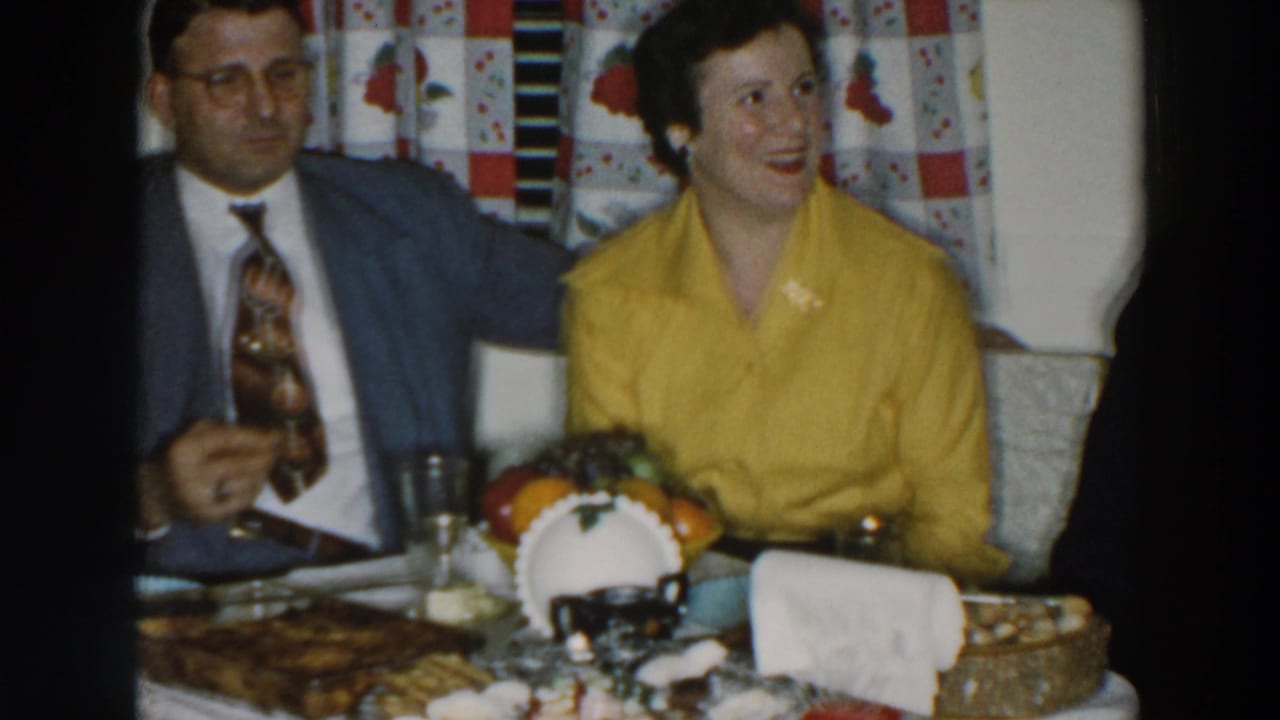 Two adults seated at a holiday table with food and a fruit centerpiece.