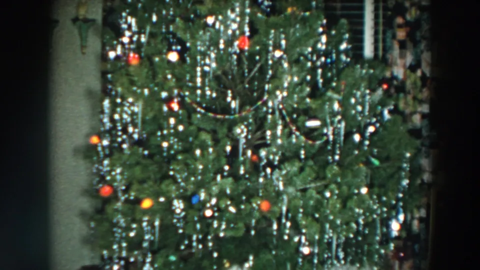 The home movie holds on the decorated Christmas tree, showing dense silver tinsel, colored bulbs, and ornaments.