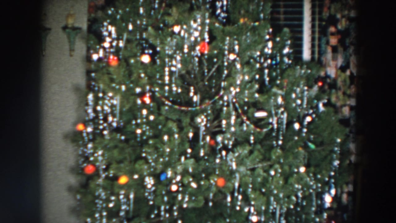 Decorated Christmas tree with tinsel, colored ornaments, and lights in a dim interior.