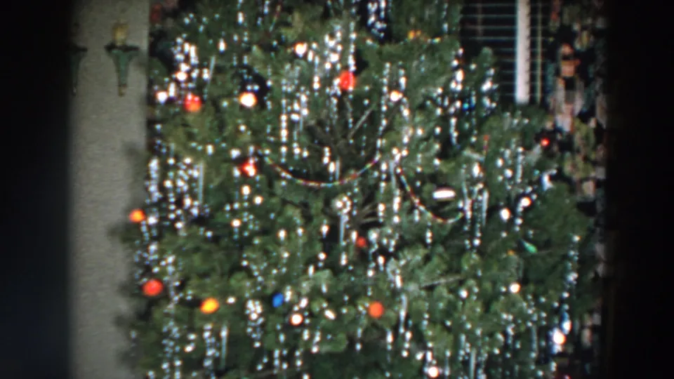 1957 Wheeling, Ohio home-movie frame showing a decorated Christmas tree with silver tinsel, colored bulbs, and ornaments in a private interior.