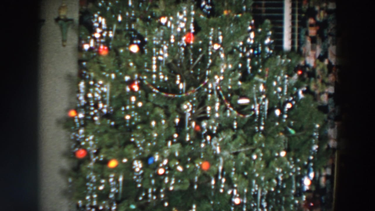 Close framing on a Christmas tree covered with silver tinsel and colored ornaments.