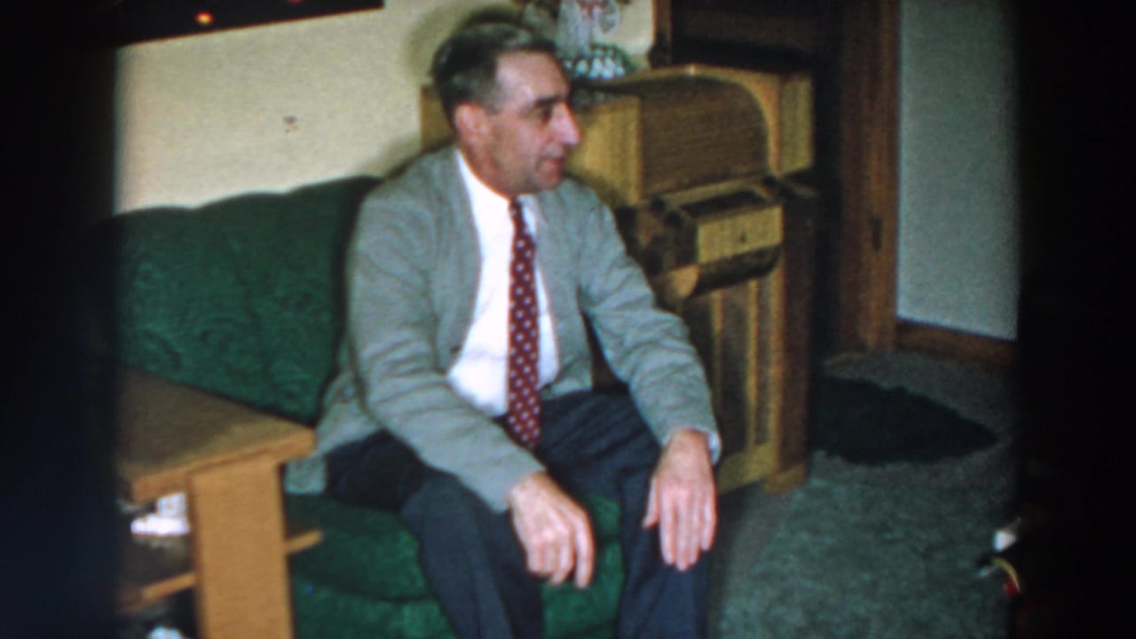 Man seated on green couch, looking right beside a wood cabinet.