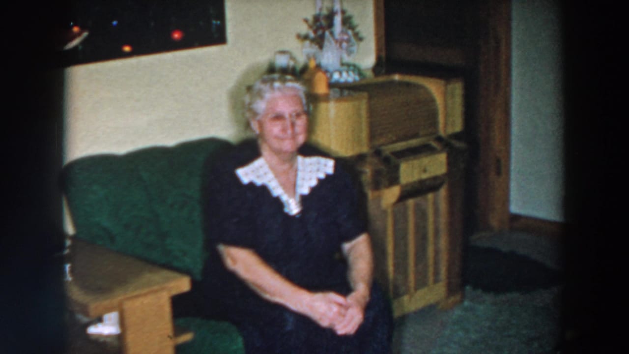 Woman seated on a green sofa with a console cabinet and small Christmas tree behind her.