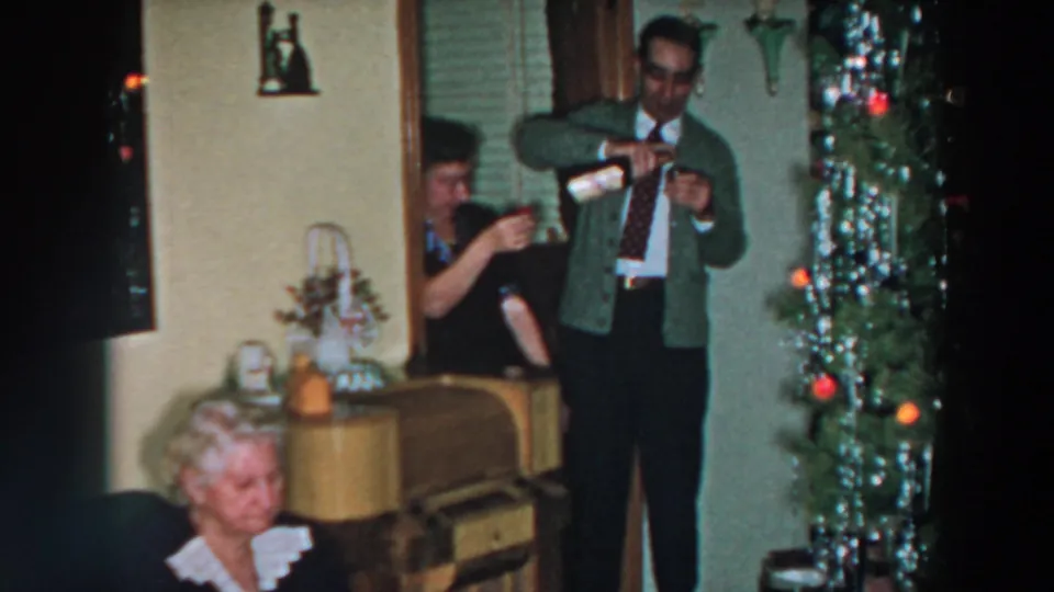 1957 Wheeling, Ohio home-movie frame of a man serving sparkling wine in a decorated private living room.