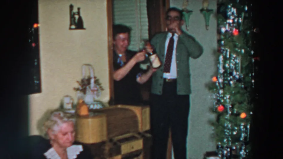 1957 Wheeling, Ohio holiday interior with a man raising a glass near a decorated Christmas tree and seated relatives.