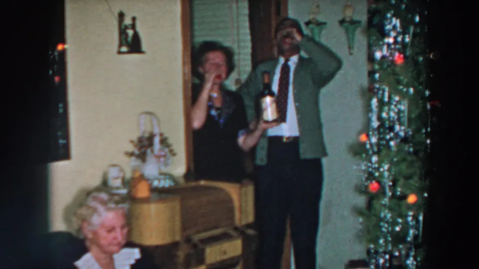 In a 1957 Wheeling, Ohio home interior, a man drinks while a woman holds a bottle beside Christmas tree decorations.