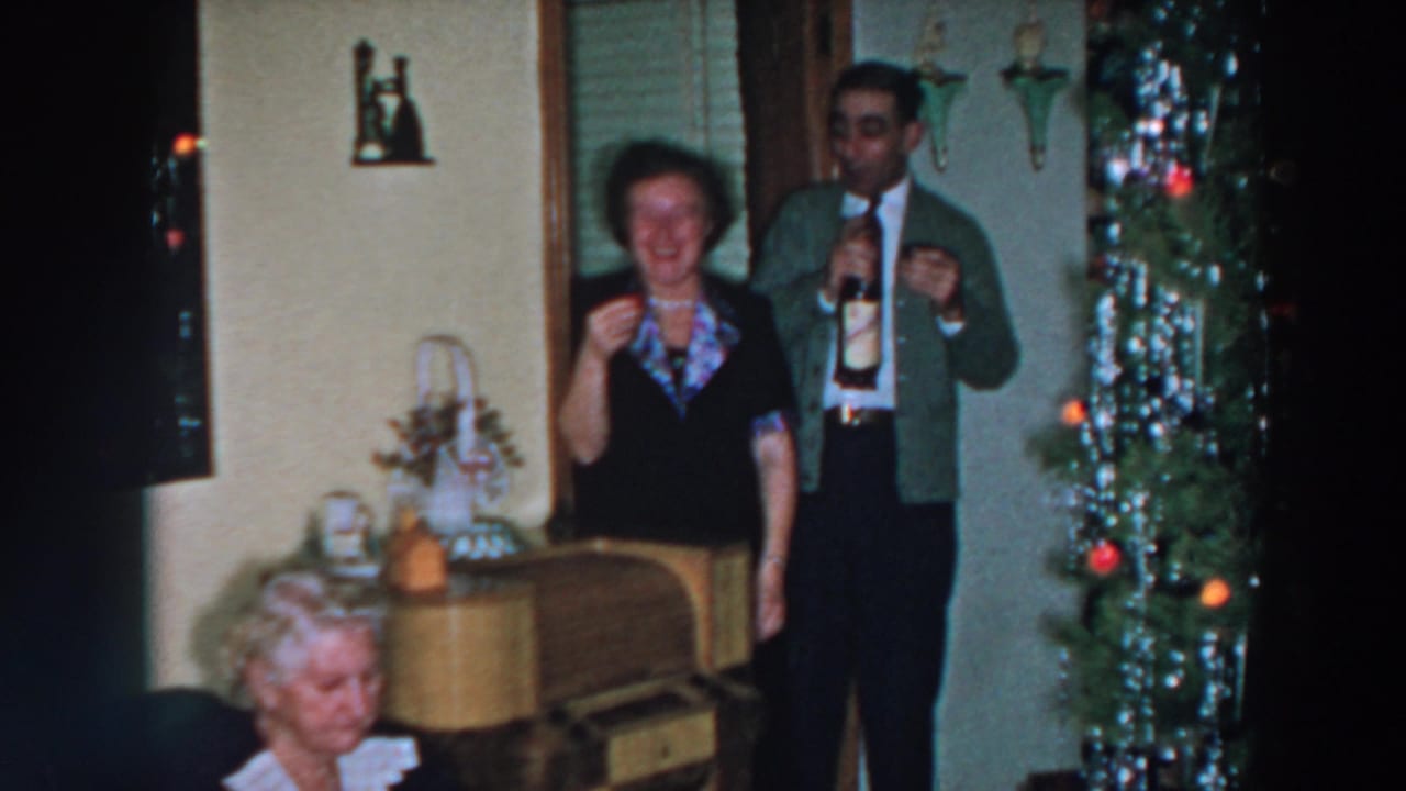 Man holding a bottle and glass beside a woman near a decorated Christmas tree.