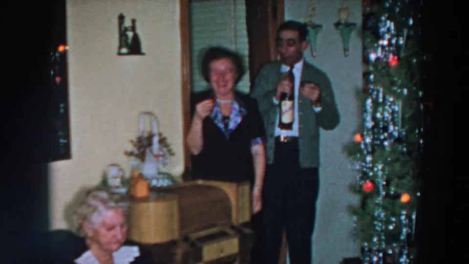 In a 1957 Wheeling, Ohio home interior, a man holds a bottle and glass while a woman smiles beside a tinsel Christmas tree.
