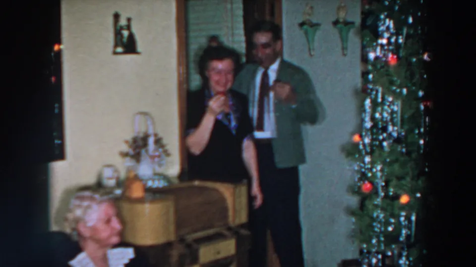 A smiling woman holds a drink as a man stands partly behind her, framed by a tinsel Christmas tree in Wheeling, Ohio, 1957.